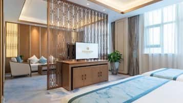 Habitación de hotel con una cama, un televisor sobre un mueble de madera, un sofá y una planta en maceta.