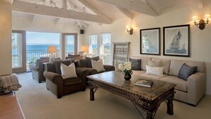 A spacious living room with a high ceiling, large windows overlooking the sea, and a cozy seating area with a coffee table. - 3860 Escabar Escape - Bay View, Old World Charm (Pacific Grove)