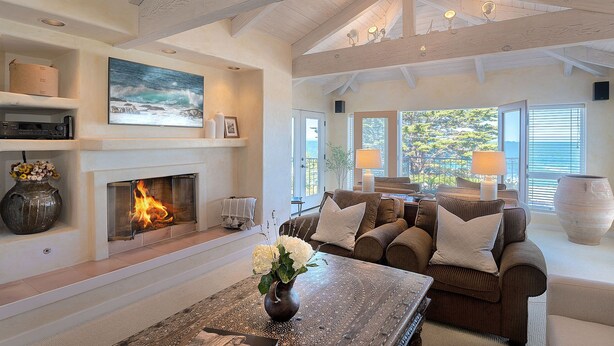 A spacious living room with a fireplace, comfortable seating, and a large window offering a view of the outdoors. - 3860 Escabar Escape - Bay View, Old World Charm (Pacific Grove)
