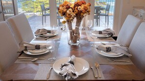 A dining table set for four with a vase of flowers, overlooking a scenic view. - 3860 Escabar Escape - Bay View, Old World Charm (Pacific Grove)