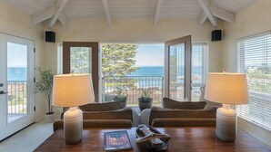 A room with two lamps, a wooden table, and a view of the ocean through large windows. - 3860 Escabar Escape - Bay View, Old World Charm (Pacific Grove)