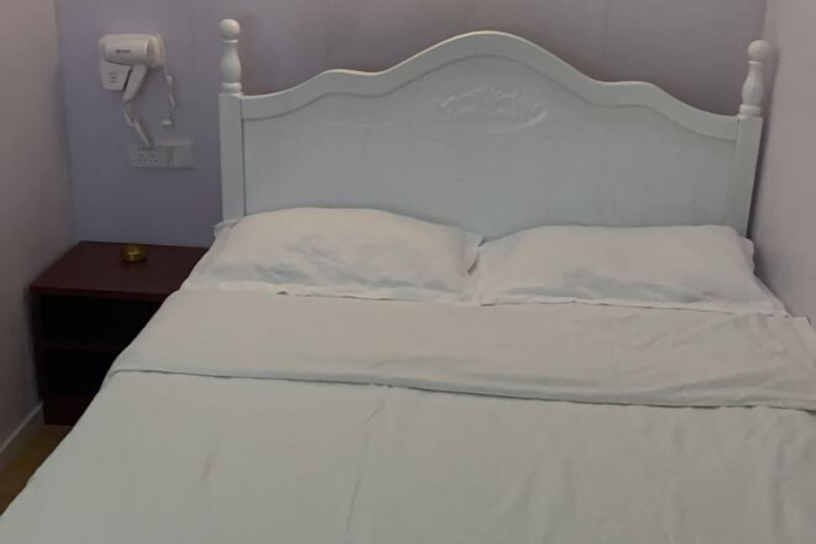 A bed with a white headboard and two pillows, a bedside table with a lamp, and a wall-mounted air purifier.