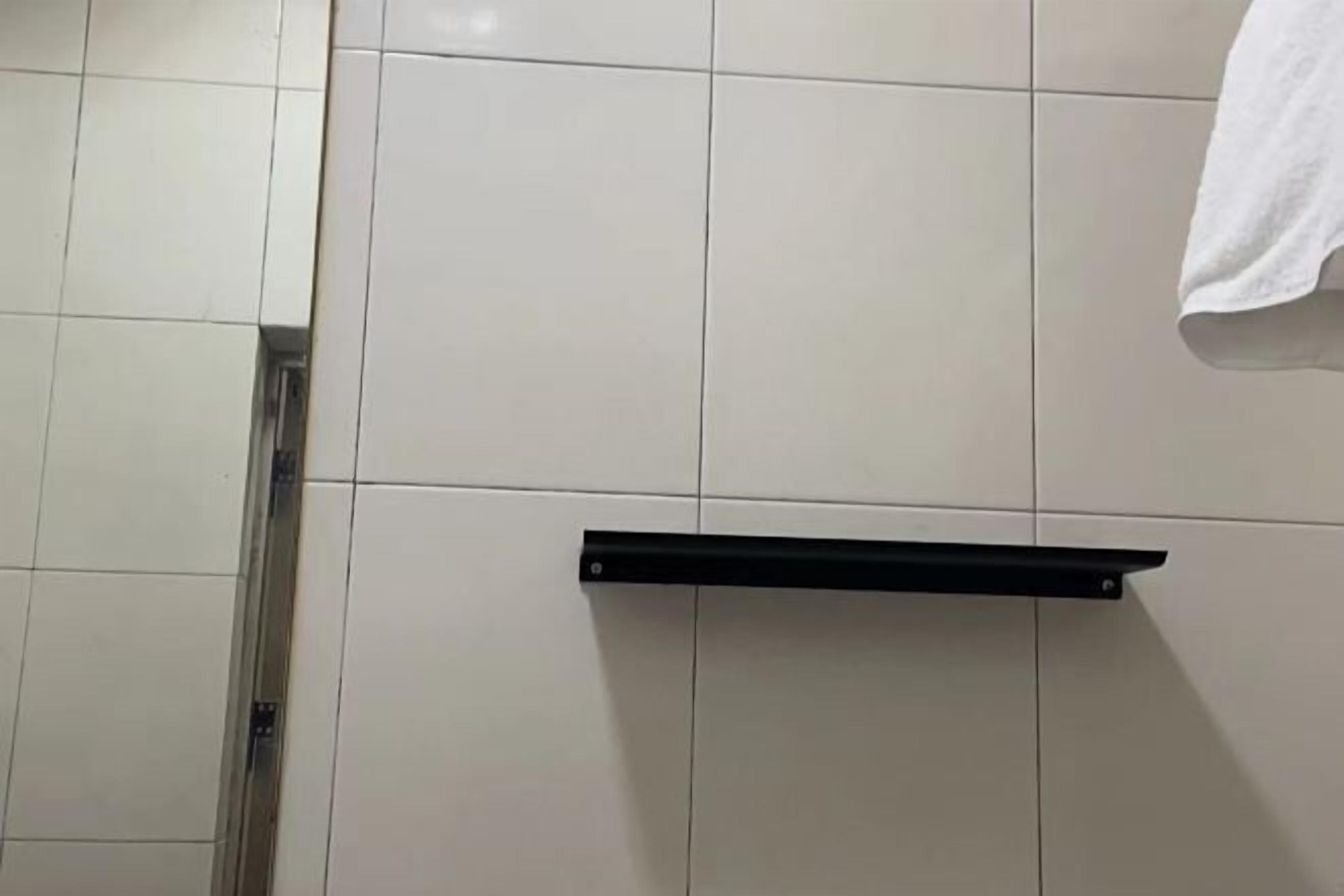 A bathroom with white tiled walls, a black towel rack, and a metal shower control panel.