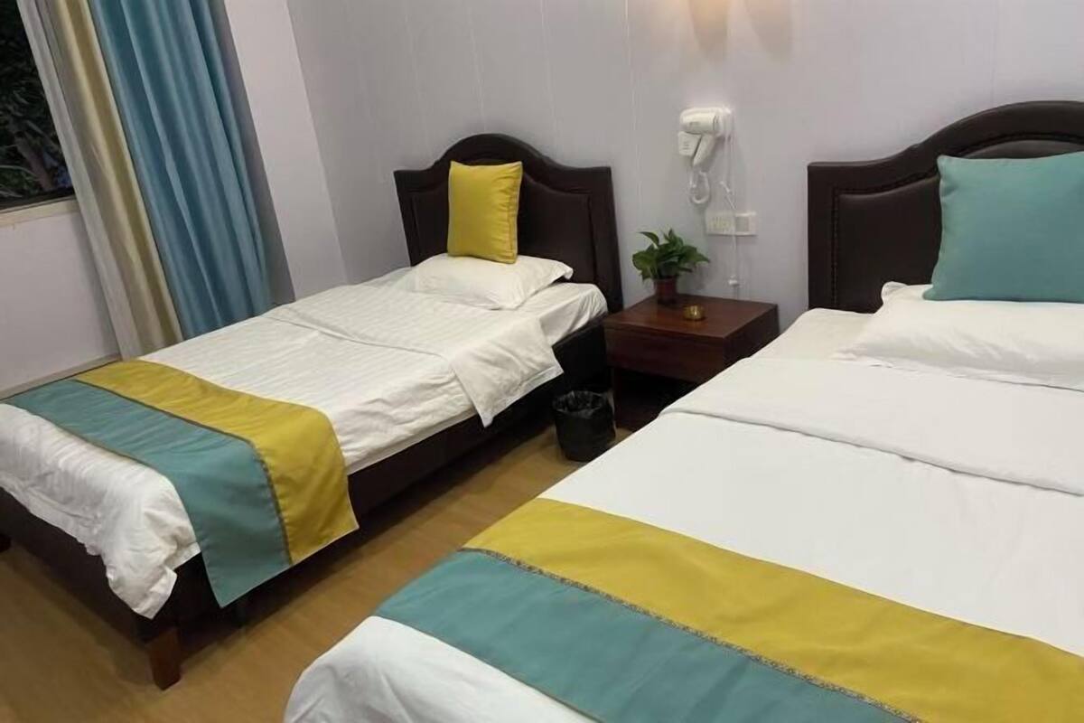 Dos camas individuales con cabeceros de madera, ropa de cama blanca y una mesita de noche con una planta y una lámpara.