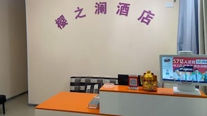 A reception area with a sign reading "Hua Zhen Liquor Store" in purple characters. There is a computer monitor displaying a webpage, a golden statue, and a small table with a box on it.