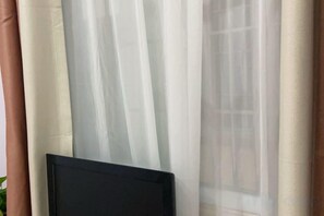 A window with sheer curtains and a dark object, possibly a TV or computer monitor, partially visible.