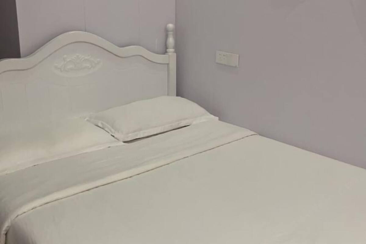 Una cama con cabecera blanca y cubrecolchón blanco.