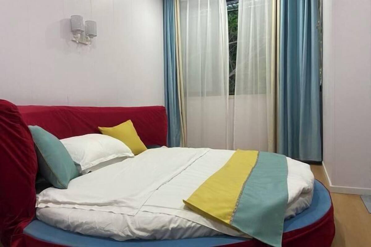 Una cama con cabecera roja, ropa de cama blanca y amarilla, y un detalle en azul.