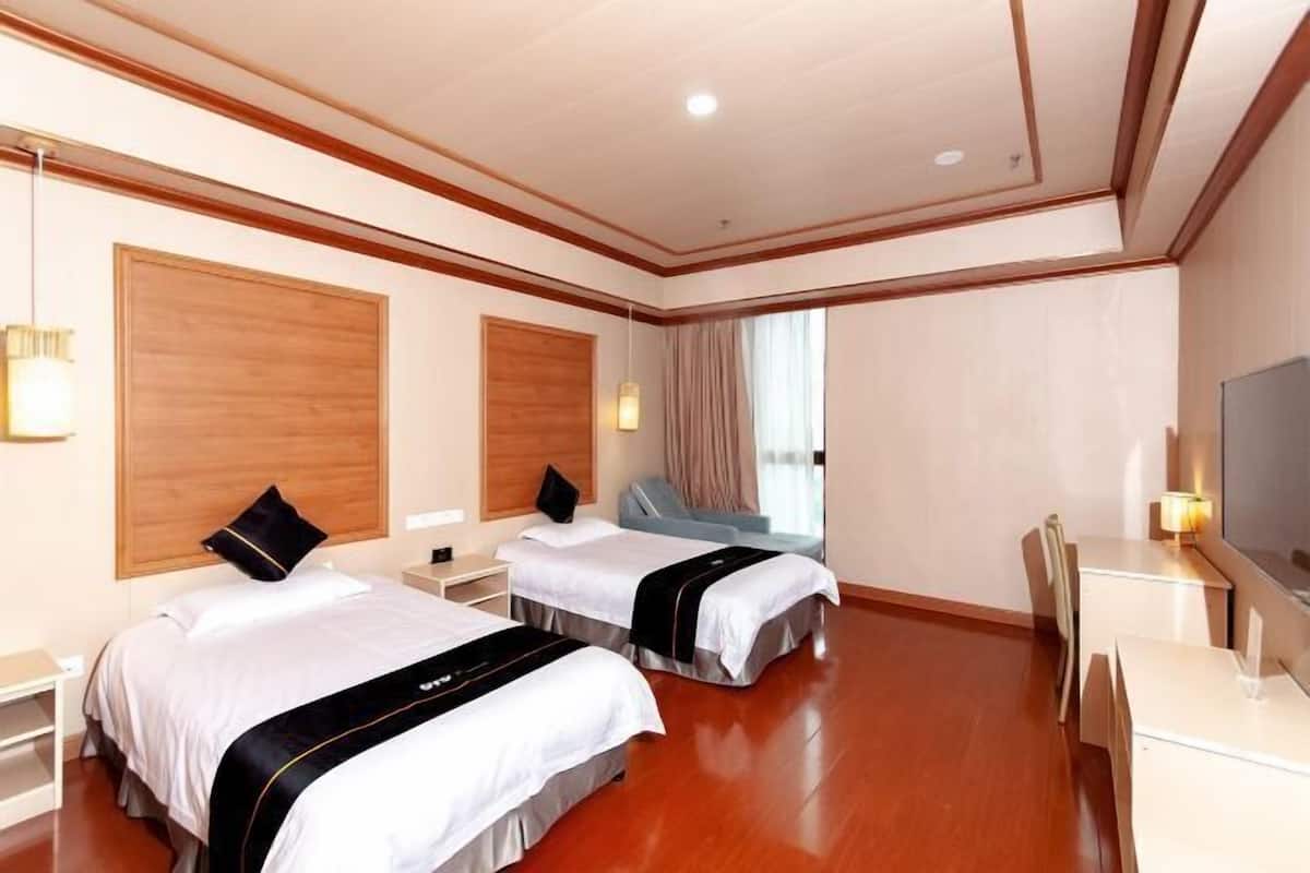 Ein Hotelzimmer mit zwei Betten, einem Schreibtisch, einem Sessel und einem Fernseher.