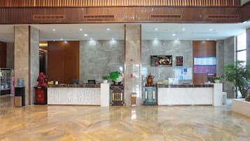 Un vestíbulo de hotel con una recepción, una planta grande y un piso de mármol.
