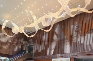 Un interior moderno con un muro de listones de madera, una escalera mecánica y un techo con lámparas colgantes.