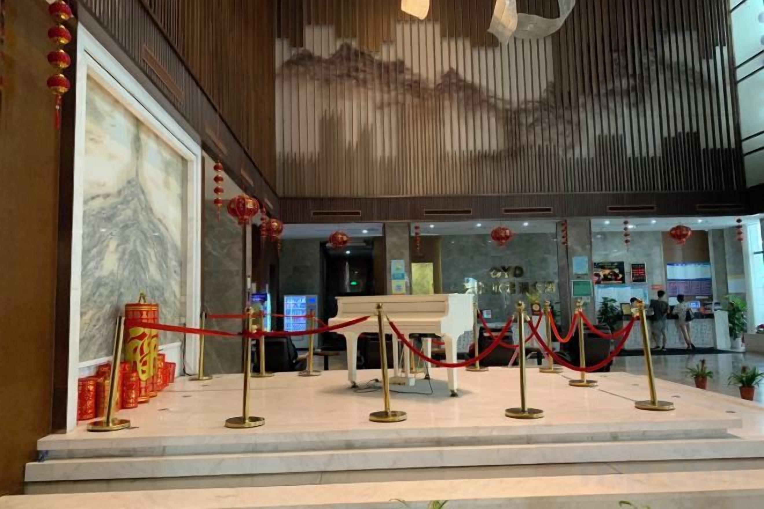 A hotel lobby with a reception desk, red velvet ropes, and a marble wall.