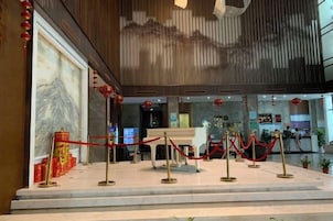 Un vestíbulo de hotel con una recepción, sogas de terciopelo rojo y una pared de mármol.