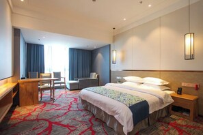 A hotel room with a large bed, a desk, a chair, and a TV.