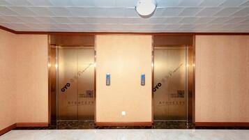 Un vestíbulo de hotel con dos ascensores, suelo de mármol y techo con detector de humo.