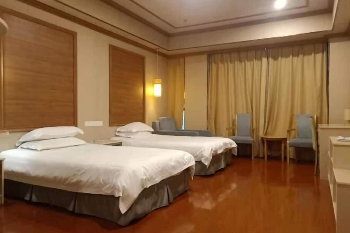Ein Hotelzimmer mit zwei Betten, einem Schreibtisch, einem Stuhl und einem mit Vorhängen versehenen Fenster.