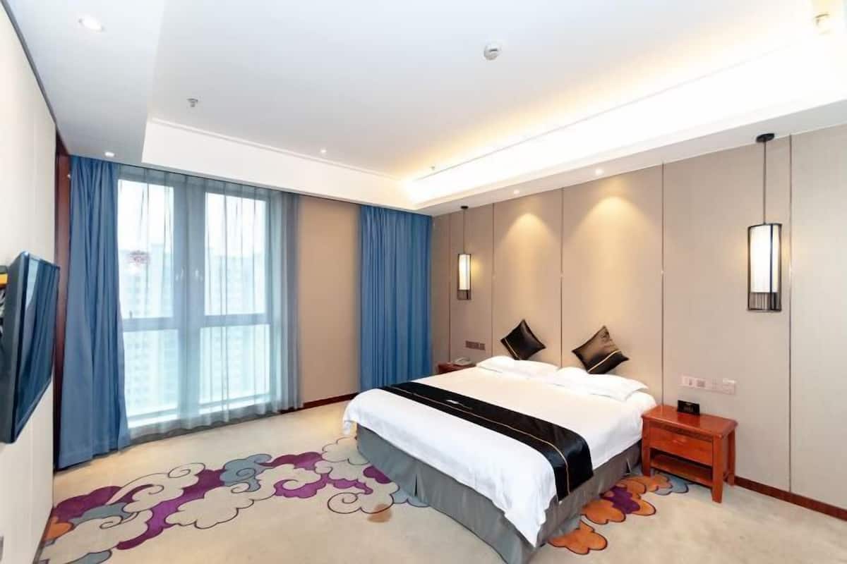 Ein modernes Hotelzimmer mit einem großen Bett, einem Flachbildfernseher, einem Nachttisch und einem großen Fenster mit Vorhängen.