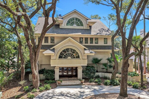 A two-story house with a prominent arched entrance, a gabled roof, and a symmetrical facade.