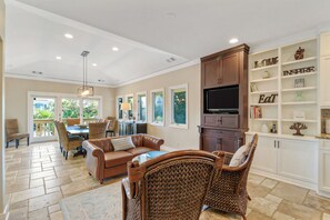 A spacious living area with a dining table, leather sofas, wicker chairs, a TV, and a bookshelf with motivational quotes.