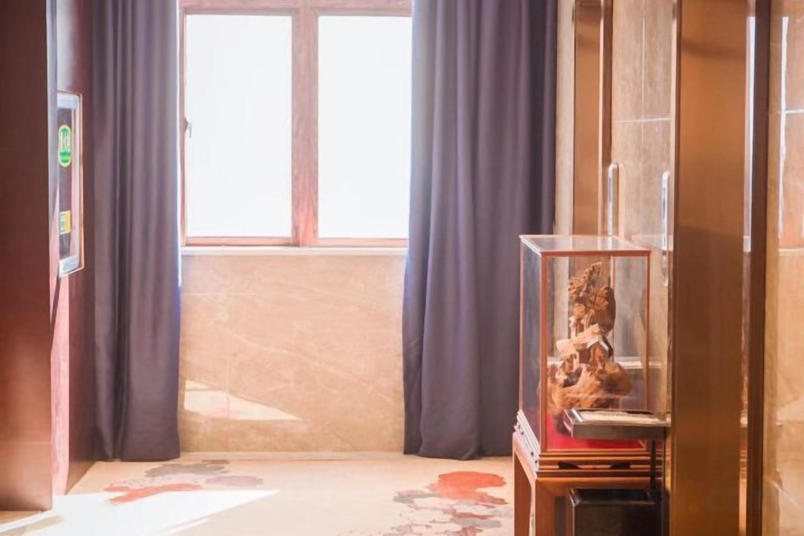 Une pièce avec une fenêtre, des rideaux, un téléviseur et un meuble contenant un objet décoratif.