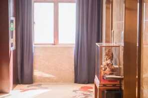 A room with a window, curtains, a television, and a cabinet with a decorative item. - Xiangdu Hotel (Jinxi)