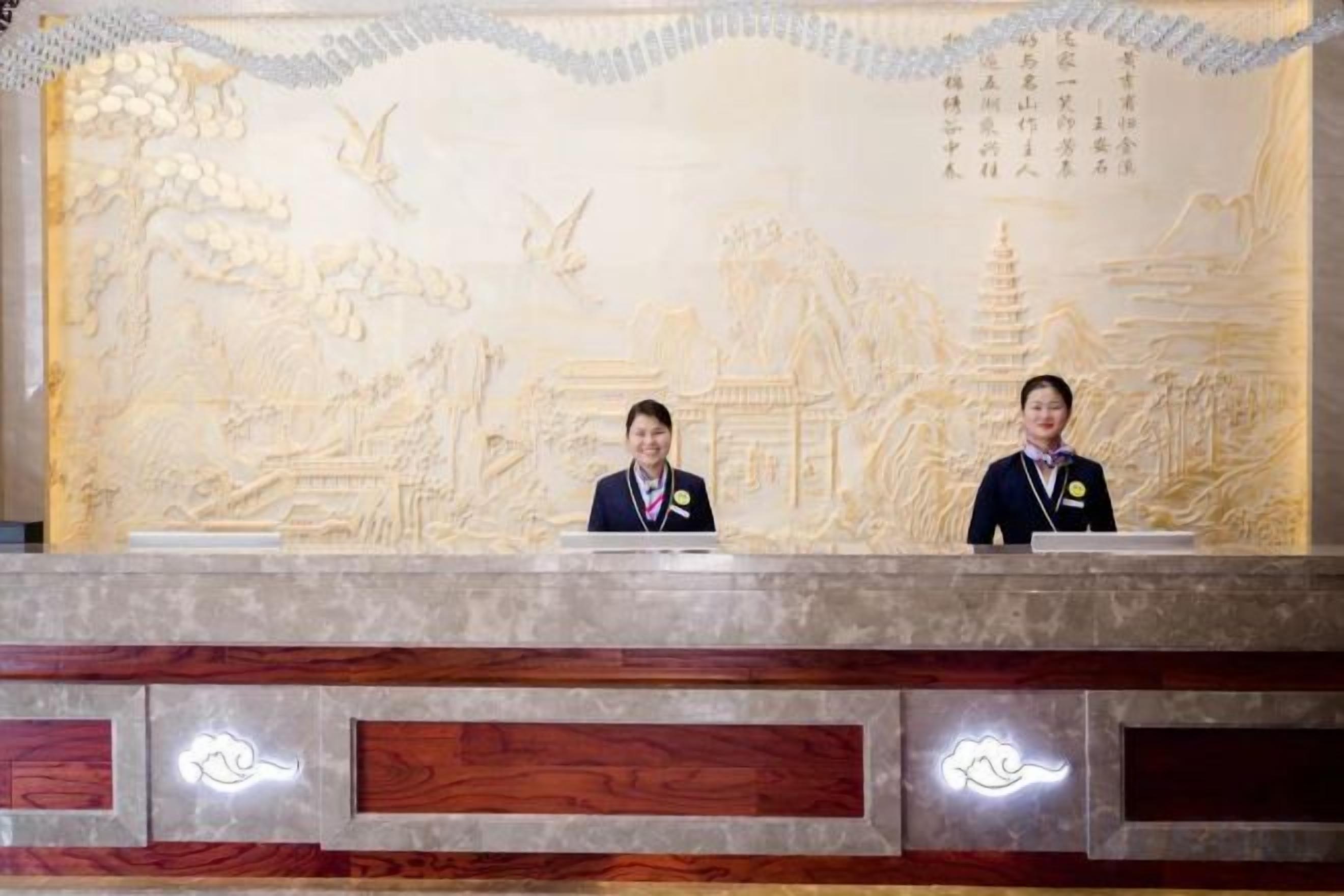Two receptionists at a reception desk with a detailed carved wall behind them.