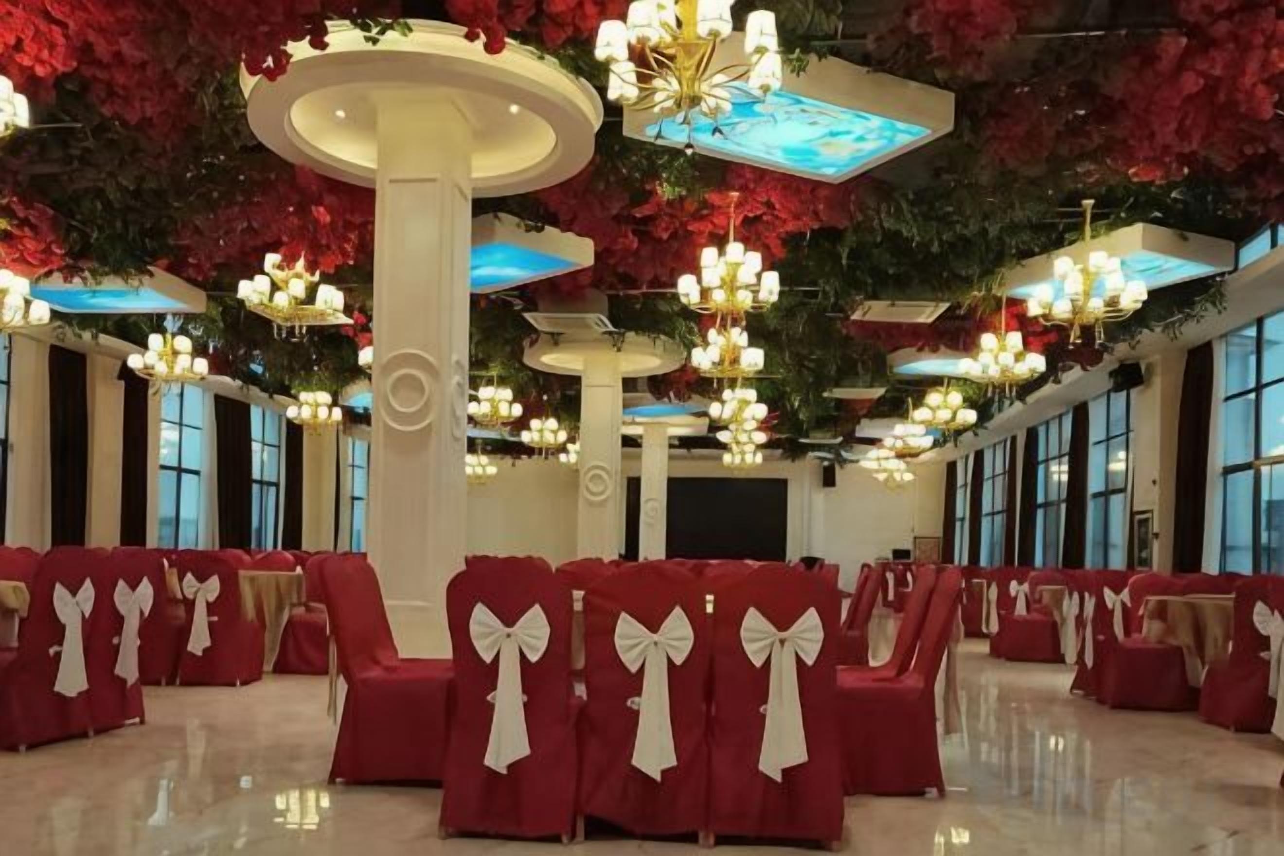 A spacious hall with rows of red chairs, large columns, and multiple chandeliers.