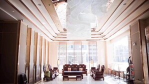 Eine großzügige Lobby mit hoher Decke, großen Fenstern und einer zentralen Sitzecke mit Sofas und Tischen.