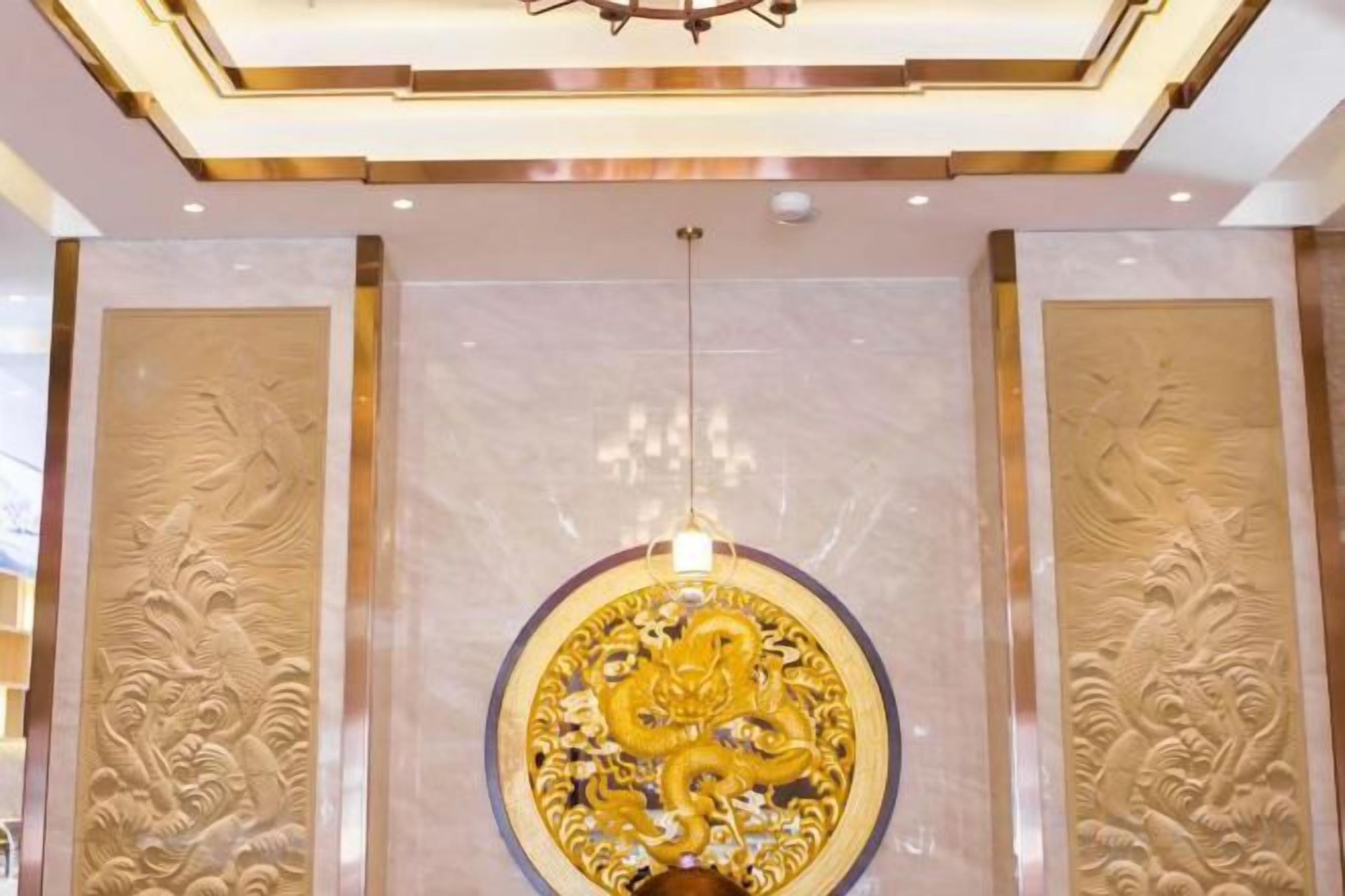 A lobby with a large circular golden emblem, a chandelier, and intricate wall carvings.