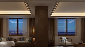 Ein Hotelzimmer mit einem großen Bett, einer Sitzecke, einem Schreibtisch und Blick auf die Stadt durch große Fenster.
