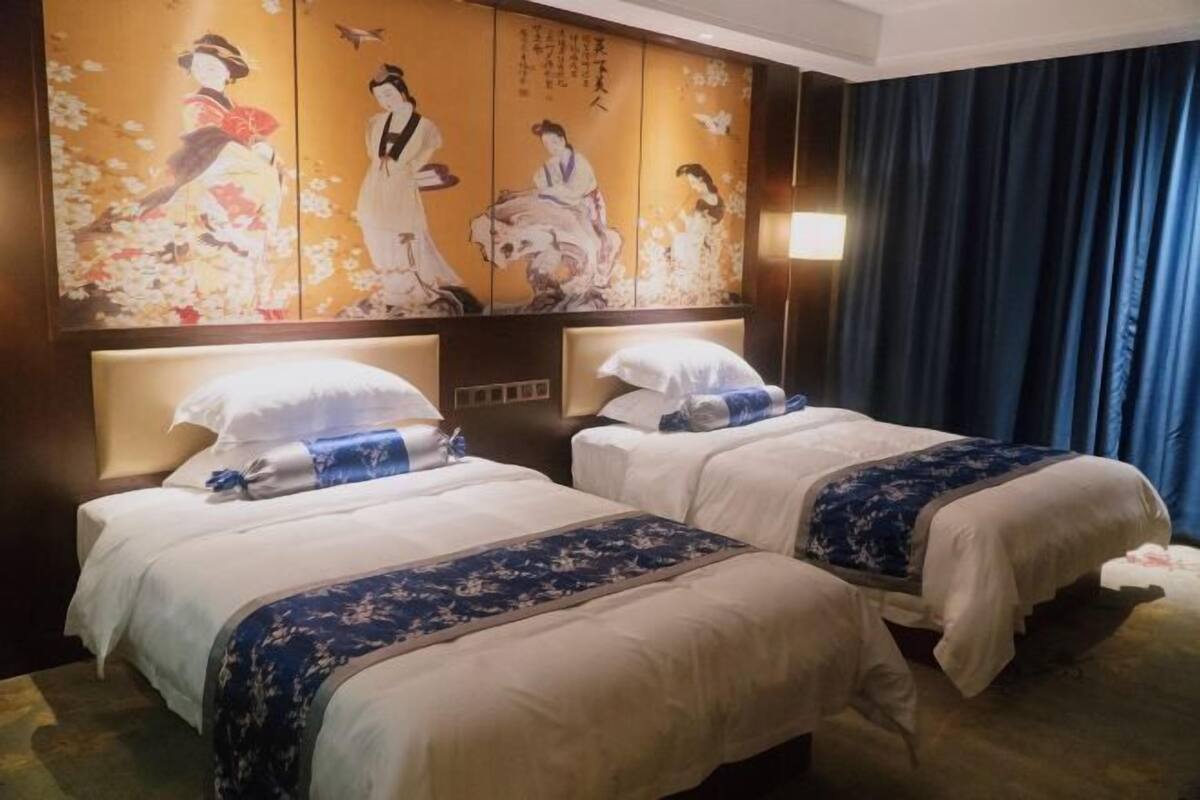 A hotel room with two beds, a traditional Japanese artwork on the wall, and a large window with curtains.