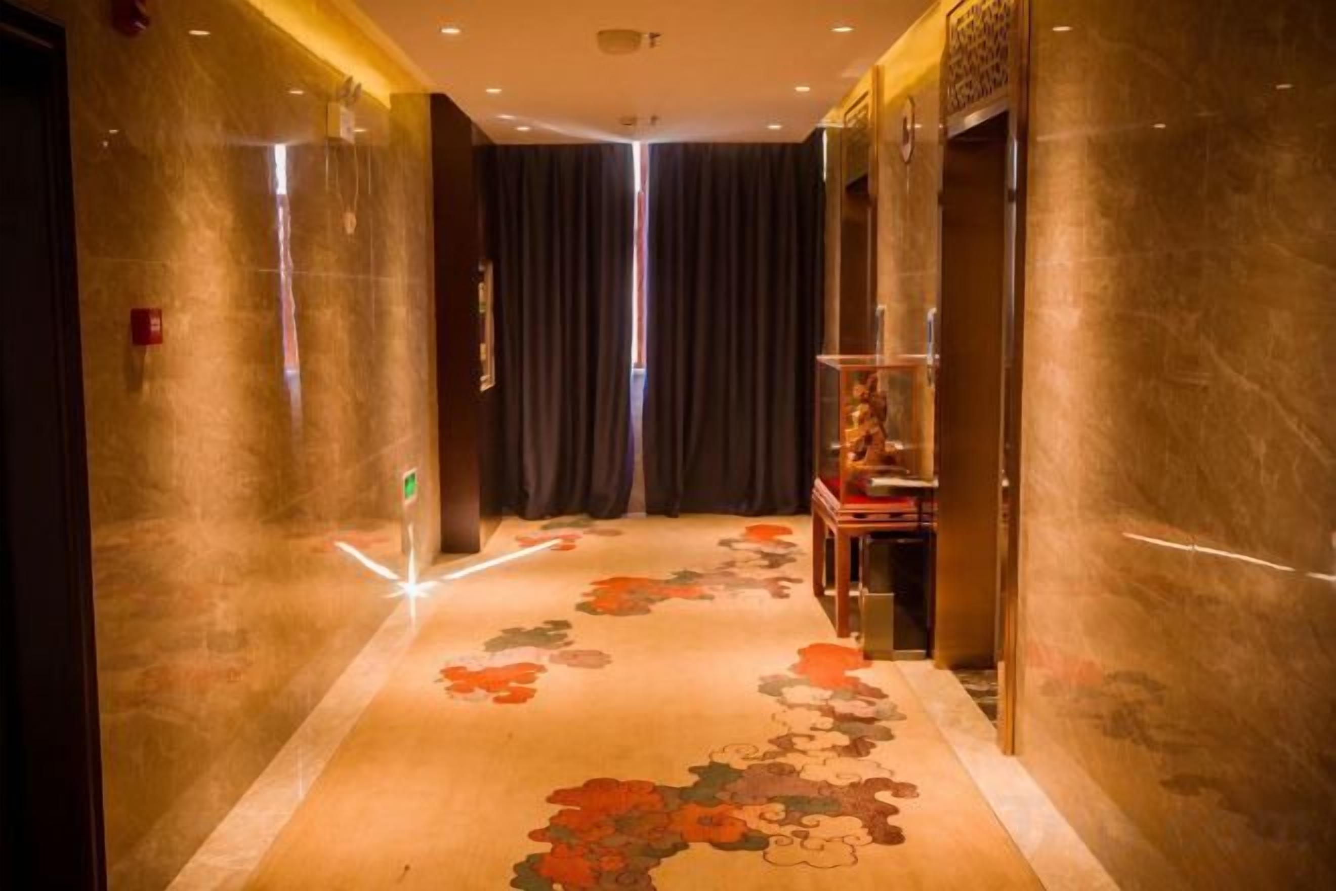 A corridor with a patterned carpet, a glass display case, and a dark curtain.