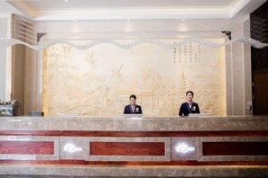 A reception desk with two staff members, a detailed wall mural, and a modern reception area. - Xiangdu Hotel (Jinxi)