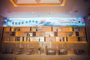A reception area with a digital display, shelves with various items, and a counter with chairs. - Xiangdu Hotel (Jinxi)