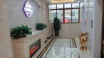A hotel lobby with a marble fireplace, potted plants, a large window, and a decorative statue.