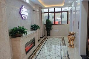 Un vestíbulo de hotel con chimenea de mármol, plantas en macetas, un ventanal grande y una estatua decorativa.