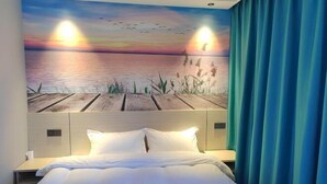 A hotel room with a bed, a headboard with a mural of a sunset over water, and a blue curtain. - JYhotel (Yuyao)