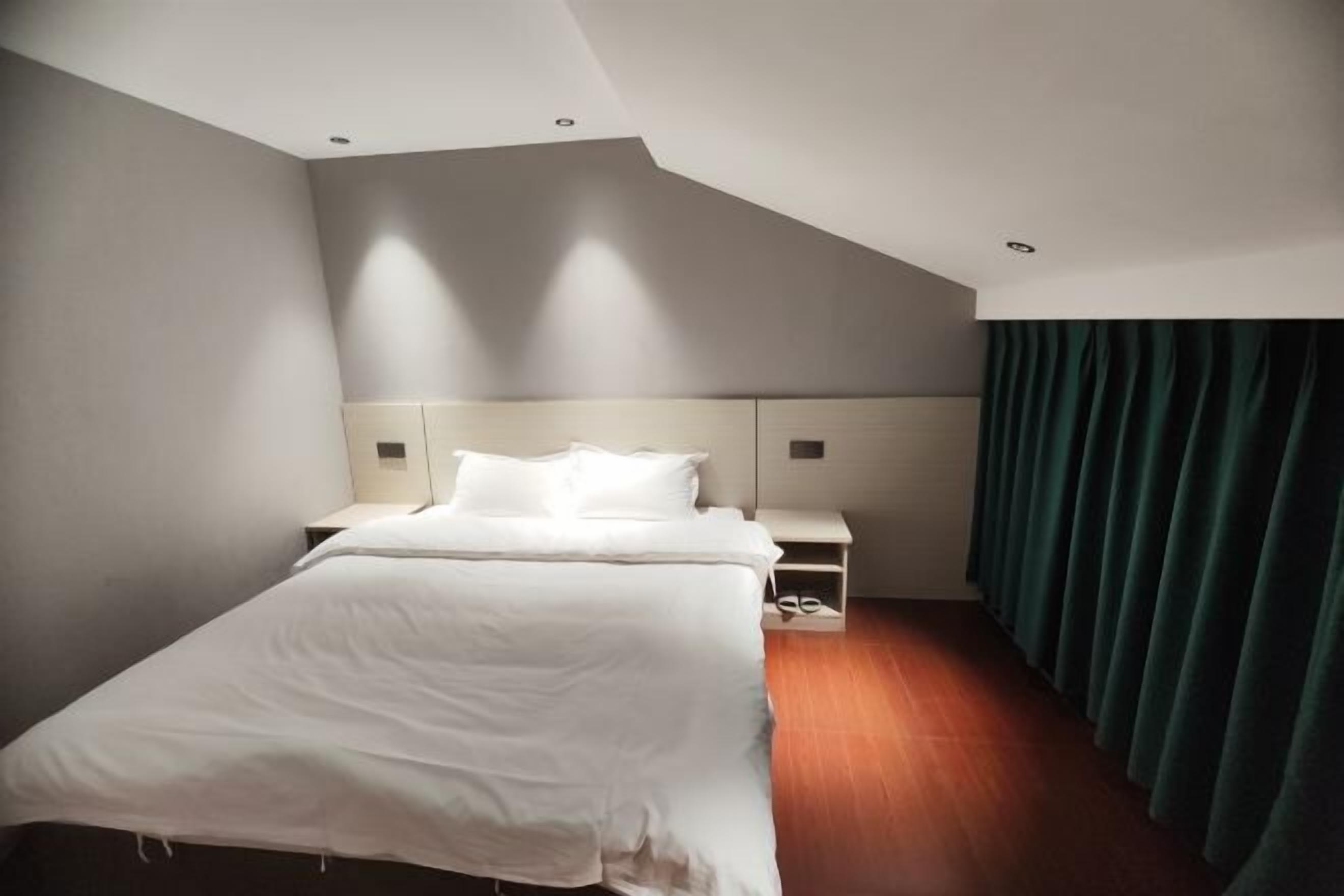 Une chambre d’hôtel avec un lit, des tables de chevet, une tête de lit et un rideau.