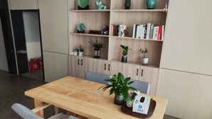 A wooden dining table with two chairs, a bookshelf with books and decorative items, and a small plant on the table. - JYhotel (Yuyao)