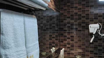 A bathroom with a tiled wall, a towel rack with towels, a hand dryer, and a glass soap dispenser.