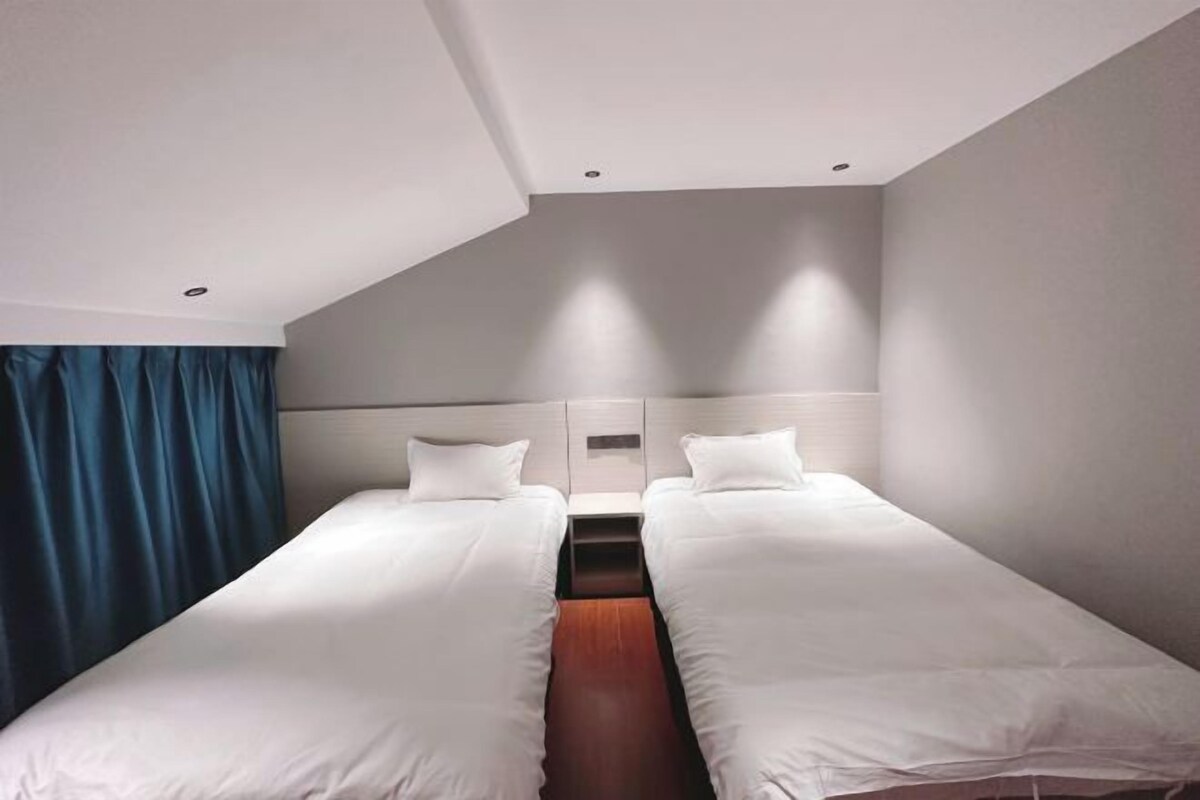 A hotel room with two single beds, a wooden floor, a white headboard, and a blue curtain.