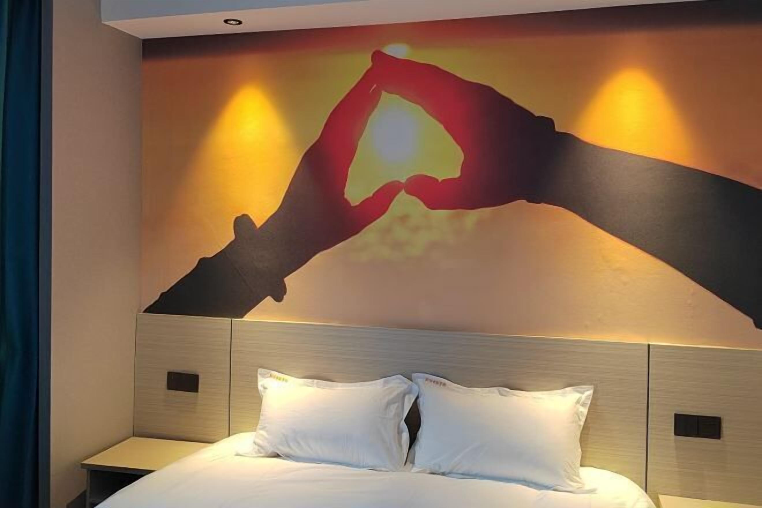 A hotel room with a bed, a nightstand, and a wall with a handprint artwork.