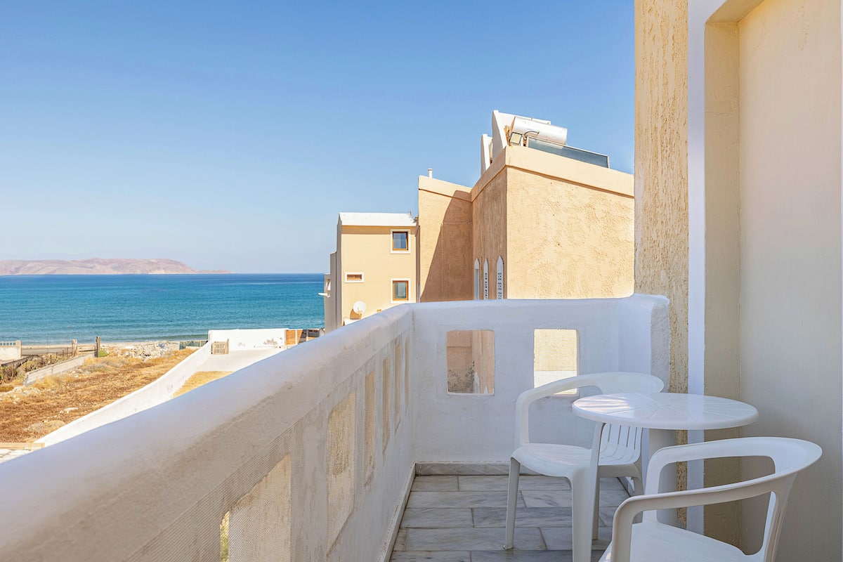 A balcony with white chairs and a view of the sea.