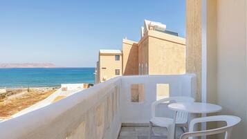 A balcony with white chairs and a view of the sea.