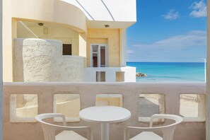 A balcony with white chairs and a table, overlooking a clear blue sea and a white building with a door. - Niros Beach (Hersonissos)