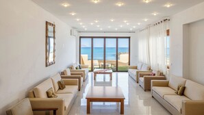 A spacious living room with a view of the beach, featuring multiple sofas, a coffee table, and ceiling lights.