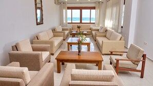 A spacious living room with beige sofas and armchairs, a wooden coffee table, and a view of the sea through large windows.