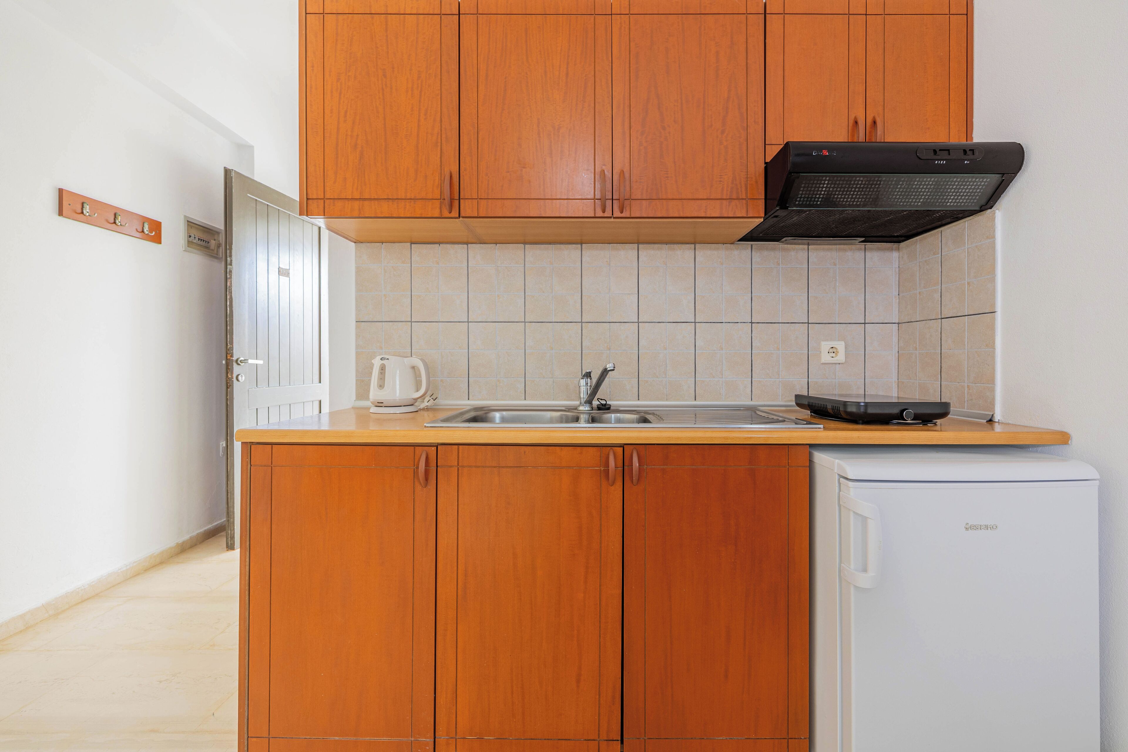 A compact kitchen with wooden cabinets, a built-in oven, a sink, and a white refrigerator.