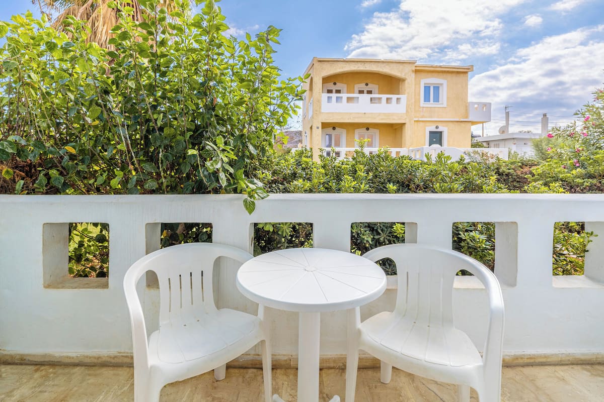 A balcony with two white plastic chairs and a small round table, surrounded by a white wall with rectangular windows.