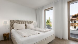 A modern hotel room with a large bed, two bedside lamps, and a view of the outside through a large window. - Apartment with 3 bedrooms and private sauna (Rohrmoos-Untertal)